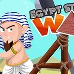 Kreslená postava s pruhovaným turbánem a plnovousem stojí vedle katapultu na pozadí s pyramidou a nápisem