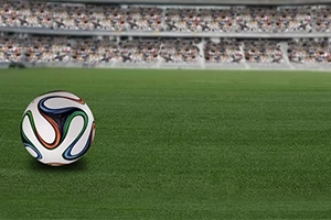 Fotbalový míč leží na zeleném trávníku před zaplněnými tribunami stadionu