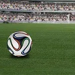 Fotbalový míč leží na zeleném trávníku před zaplněnými tribunami stadionu