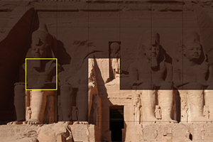 Kamenné sochy faraonů vytesané do skalního útesu s postavami sedících velikánů a hieroglyfy